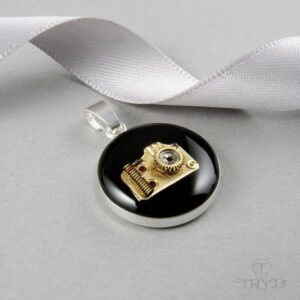 Srebrna zawieszka z aparatem fotograficznym w kolorze złotym na czarnym tle