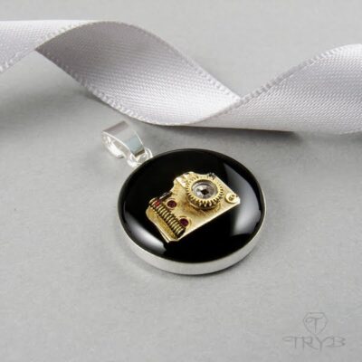 Srebrna zawieszka z aparatem fotograficznym w kolorze złotym na czarnym tle