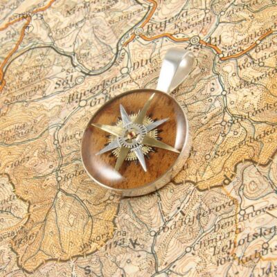 Artystyczny wisiorek róża wiatrów z części zegarków na tle drewna